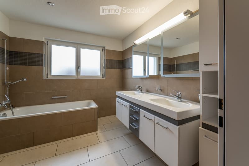 Modern bathroom with a bathtub, double sink, large mirror, and built-in cabinets.