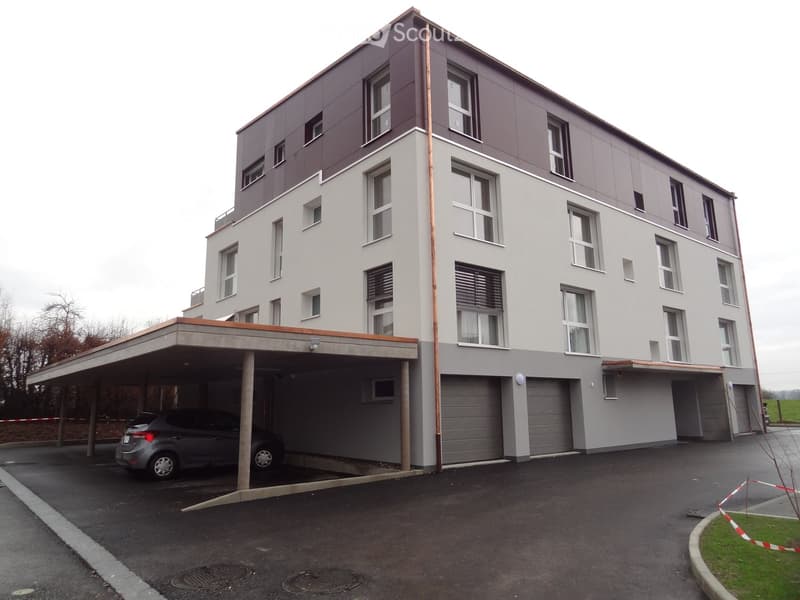 Modern multi-story building with a covered parking area and garage, featuring large windows and a clean, contemporary design.