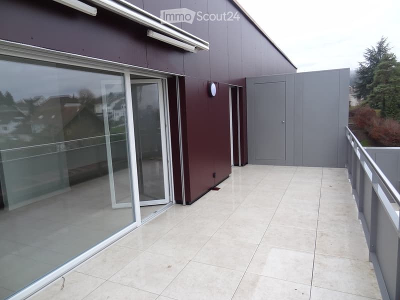 Modern balcony with large glass sliding doors, tiled floor, metal railing, and view of surrounding houses and trees.