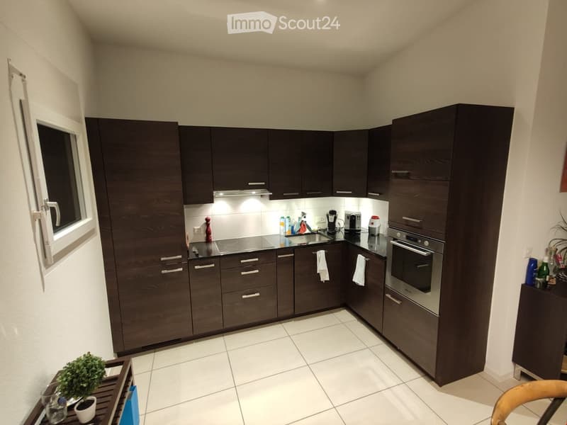 Modern kitchen with dark wooden cabinets, stainless steel appliances, and a tiled floor. Features an oven, coffee maker, and various kitchen items on the counter.