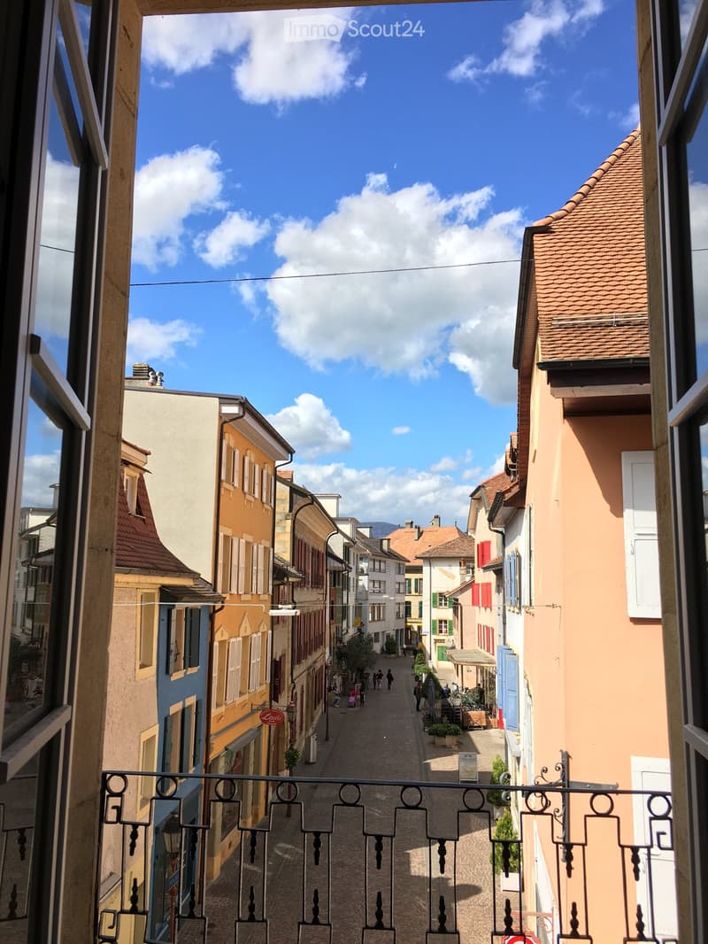 Balcony overlooking a narrow cobblestone street lined with colorful buildings, featuring shutters and small storefronts.
