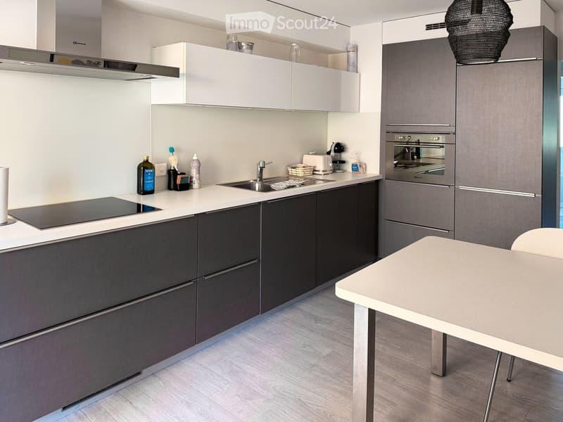 Modern kitchen with white and grey cabinets, a central island, and a dining area. Features include a sink, faucet, oven, and various small appliances.