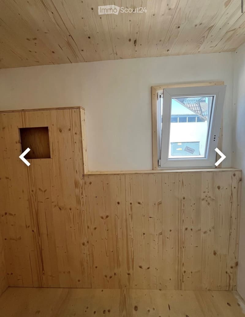 Empty room with wooden walls and ceiling, a small window, and a built-in wooden shelf unit.