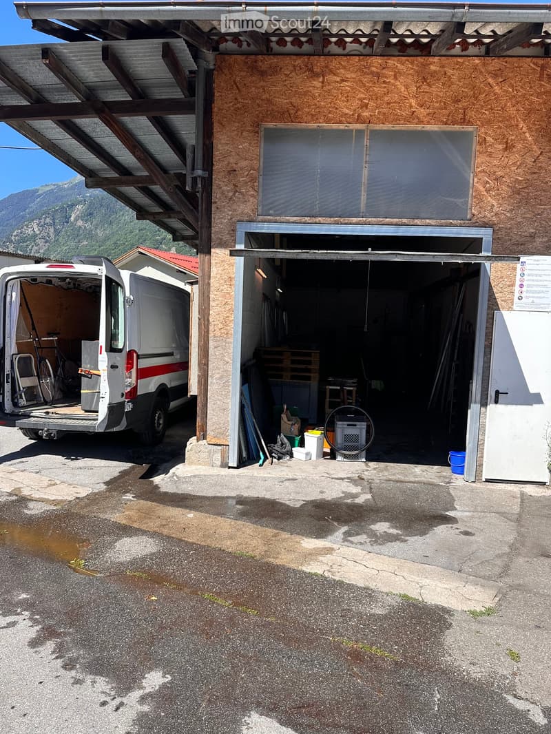 A building with a covered garage area, a van parked nearby, and various tools and materials inside the garage.
