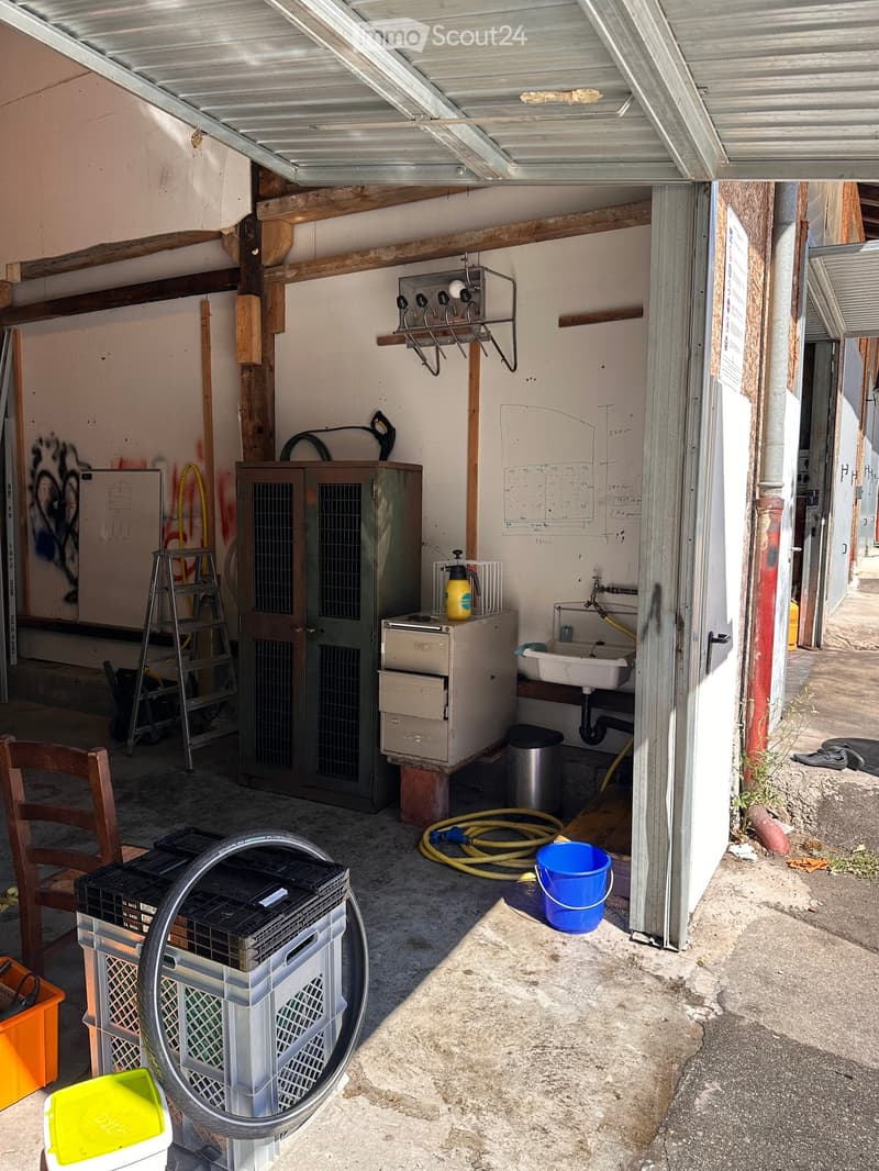 The image shows a garage or utility room with a sink, a cabinet, a chair, a ladder, and various storage items including crates and a bucket.