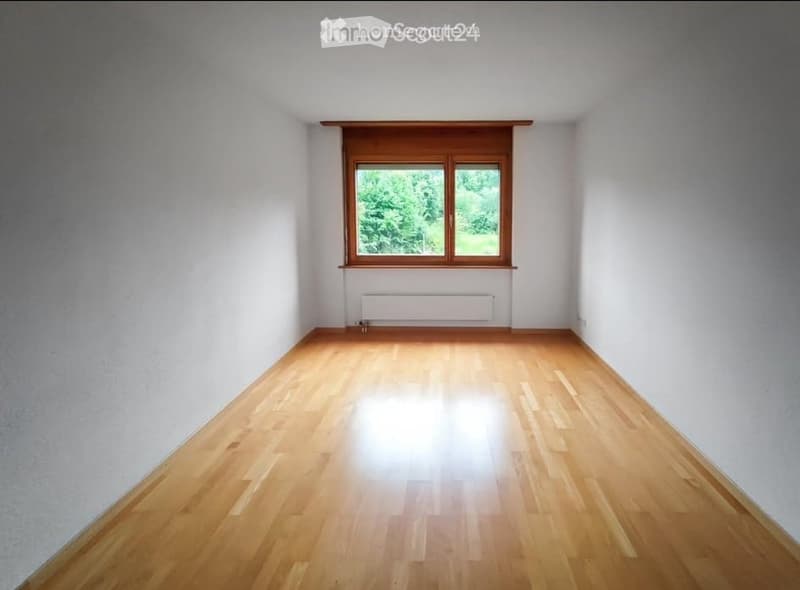 Empty room with wooden flooring, white walls, and a large window with wooden frame and radiator below.