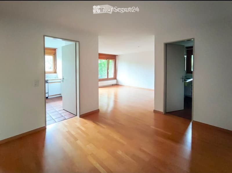 Empty room with wooden flooring and white walls, featuring three open doorways leading to other rooms.