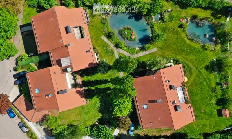 Aerial view of a residential complex with three buildings, surrounded by green lawns, trees, and a small swimming pool.