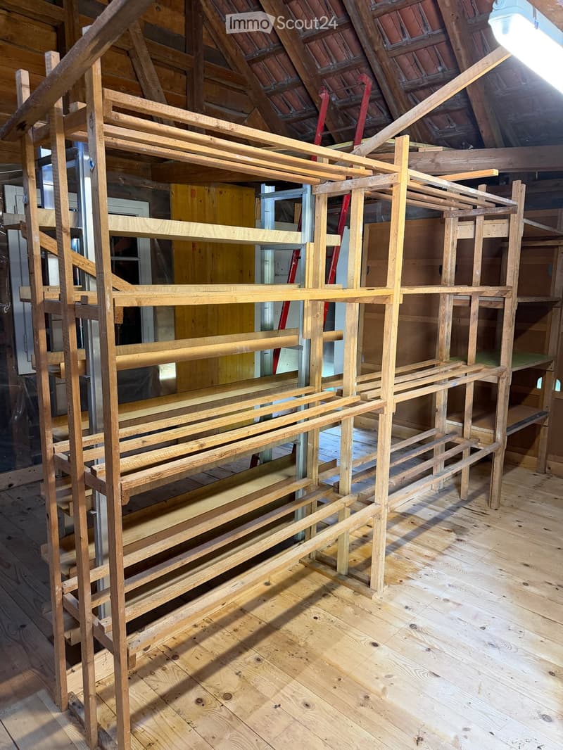 An attic space with exposed wooden beams and a wooden floor, featuring a large wooden bed frame under construction.