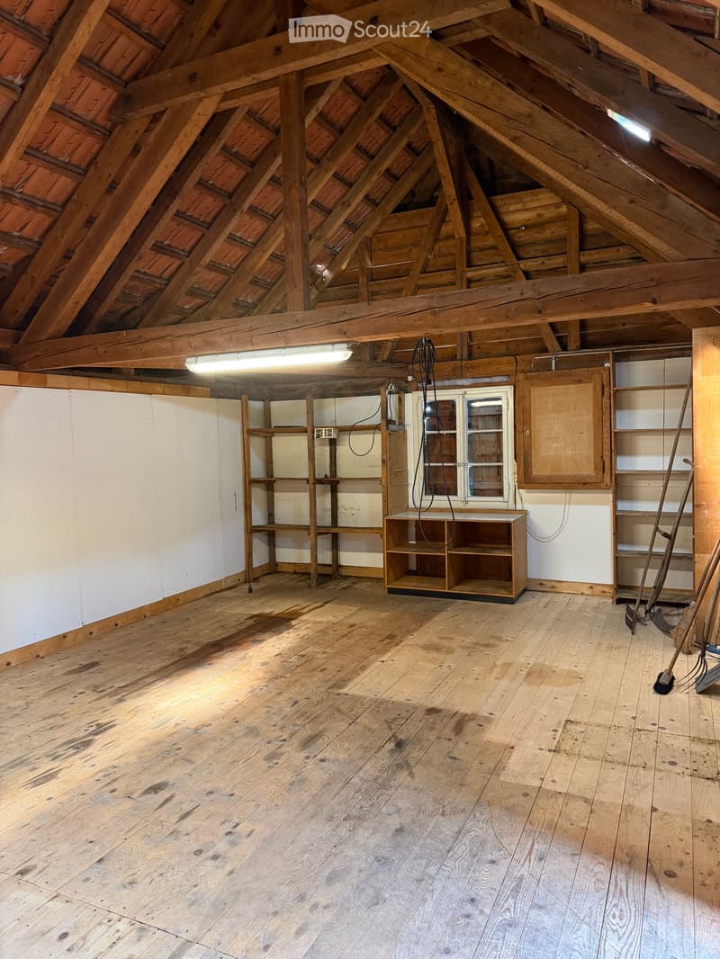 An attic space with wooden beams, exposed wooden floor, and minimal built-in shelving units. The room is empty, with no furniture or personal items.