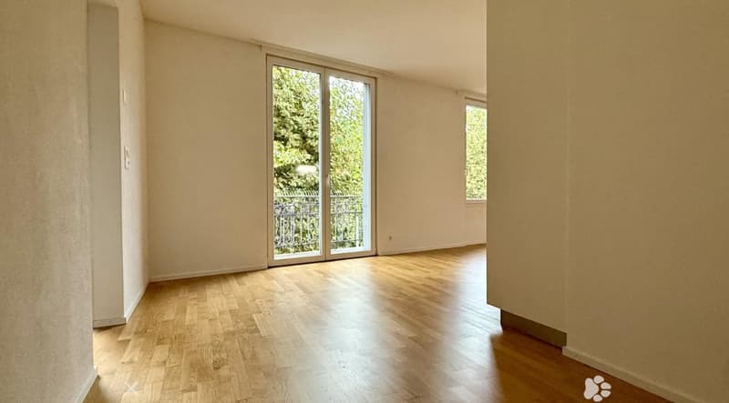 Empty room with wooden flooring, large sliding glass door leading to a balcony, and a small window on the adjacent wall.