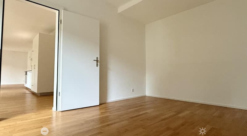 Empty room with wooden flooring, white walls, and a closed white door leading to another area.