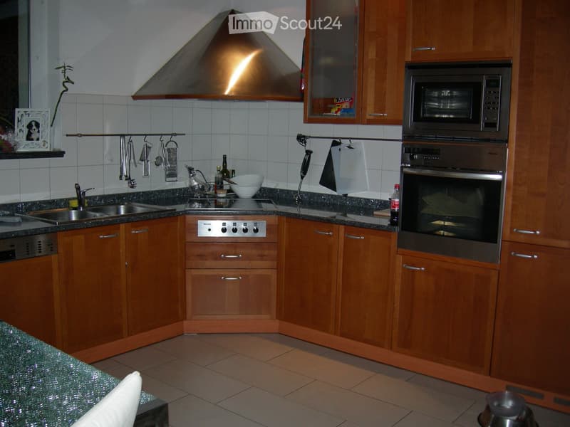 Modern kitchen with wooden cabinets, stainless steel appliances, granite countertops, and a stainless steel range hood.