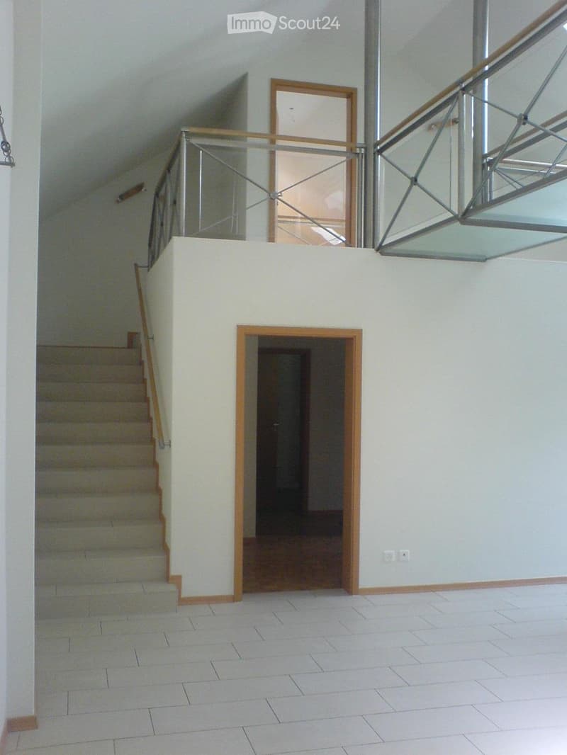 Empty hallway with tiled floor, staircase leading upwards, glass railing, and a closed wooden door.