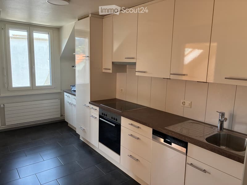 Modern kitchen with white cabinets, dark countertops, stainless steel sink, and built-in appliances including an oven and dishwasher.