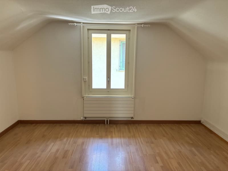 Empty room with wooden flooring, white walls, and a large window with double glass doors. A radiator is visible below the window.