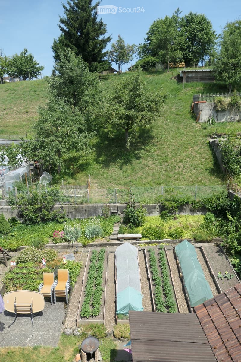 Garden with raised beds, greenhouse, patio furniture, and surrounding greenery.