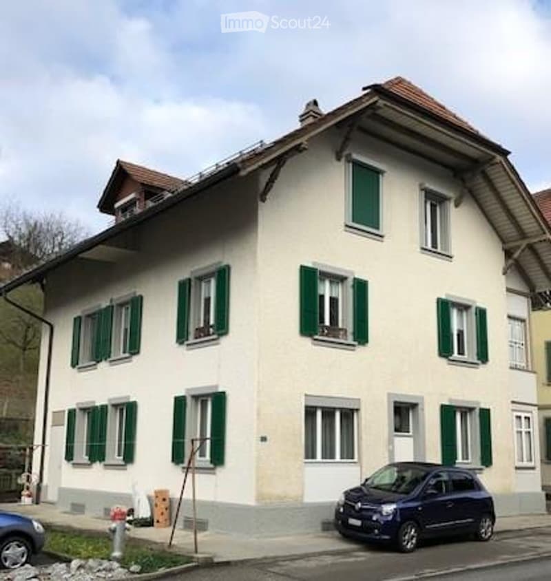 Two-story house with white walls, green shutters, and a dark blue car parked in front.