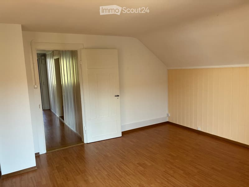 Empty room with wooden flooring, white walls, and a door leading to another area.