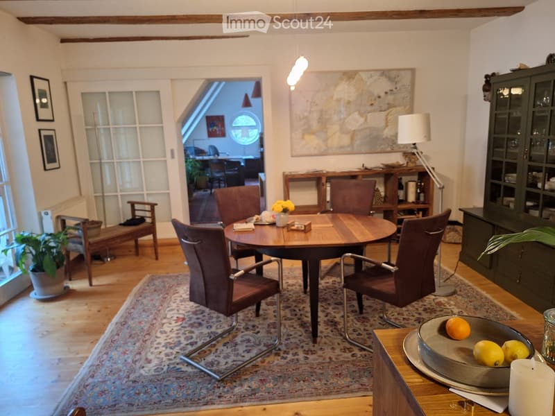 Dining area with a round wooden table, six chairs, a bench, a potted plant, a floor lamp, and a cabinet with glass doors.