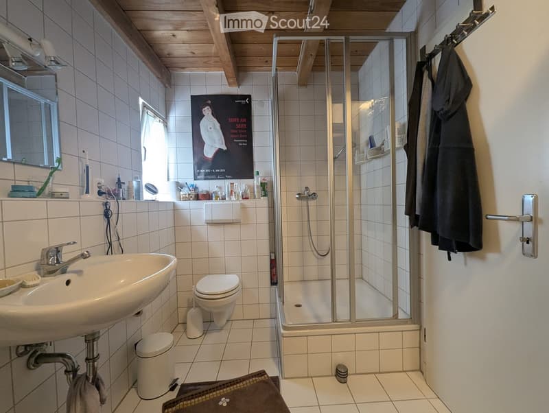 Bathroom with white tiles, a sink, toilet, shower, mirror, and various toiletries on the counter.