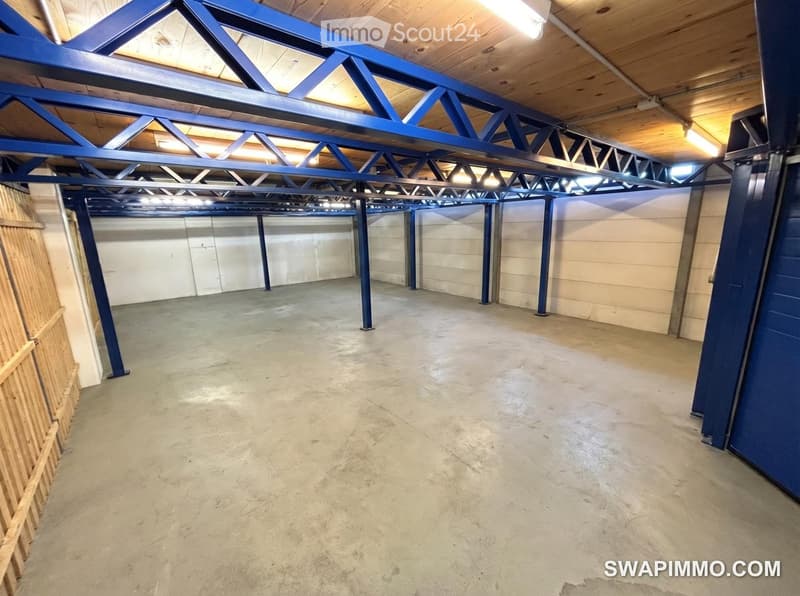 Empty garage with concrete floor, exposed wooden ceiling beams, and blue metal support structures.