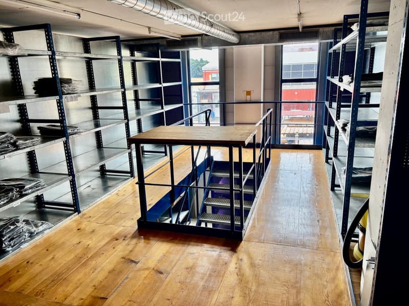 Empty room with wooden flooring, metal shelving units, and a staircase leading to an upper level. The space is clean and unfurnished.