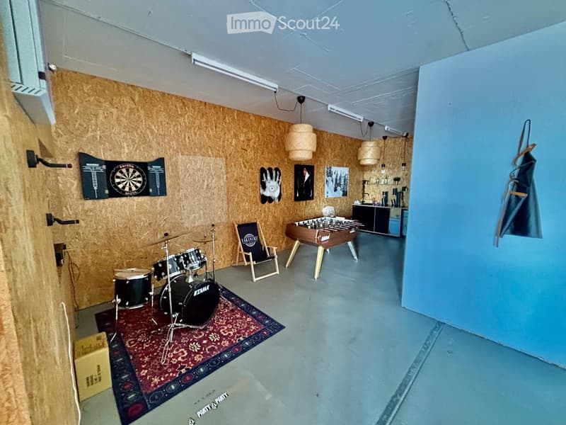 A spacious room with wooden walls, a drum set, a foosball table, a dartboard, and a small kitchen area.