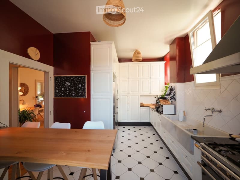 Modern kitchen with white cabinets, dark red walls, white tiled backsplash, and a wooden dining table with stools.