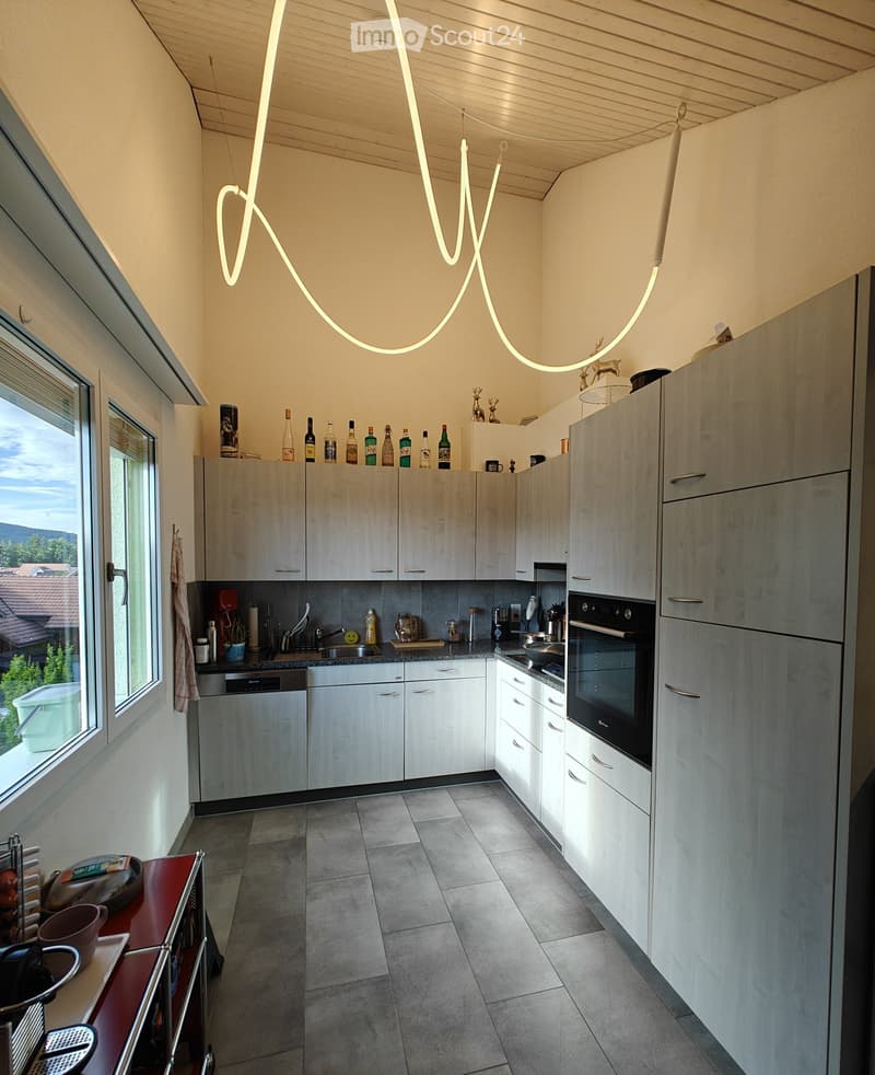 Modern kitchen with light wood cabinets, stainless steel appliances, and a large window offering a view of the outdoors.