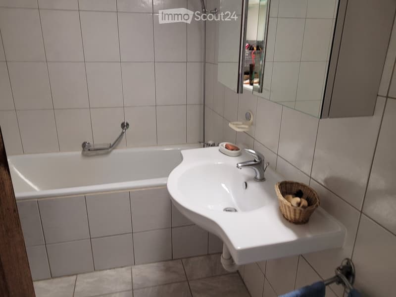 Bathroom with a bathtub, sink, mirror, and a small wicker basket on the sink counter.