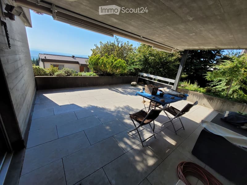 Balcony with tiled floor, table, chairs, and a view of greenery and the sea.