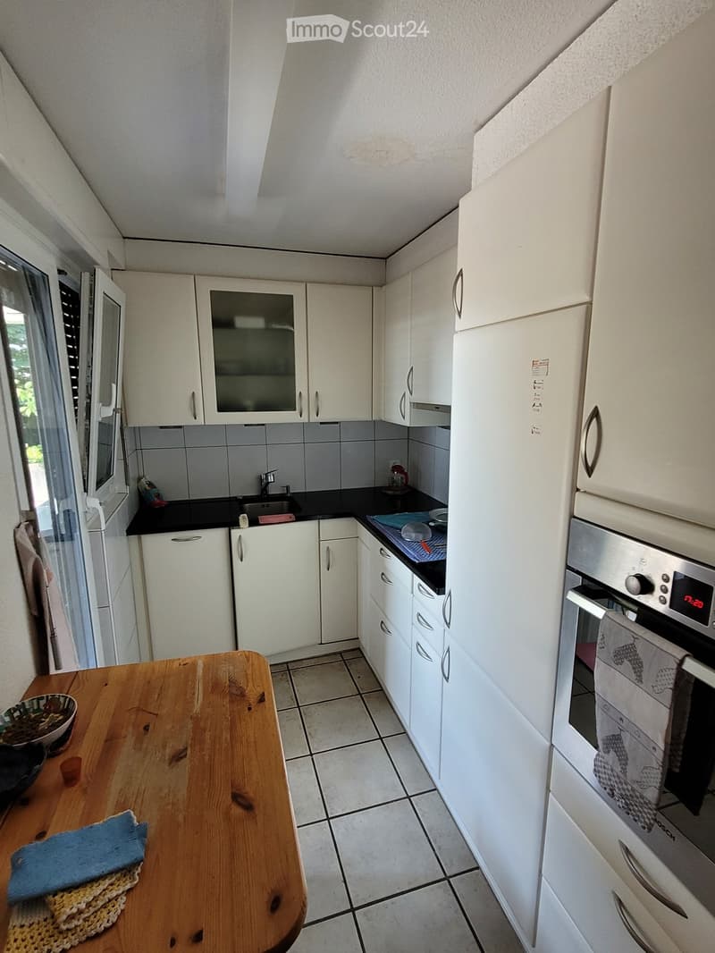 Modern kitchen with white cabinets, stainless steel appliances, and a wooden table with a bowl and oven mitt.