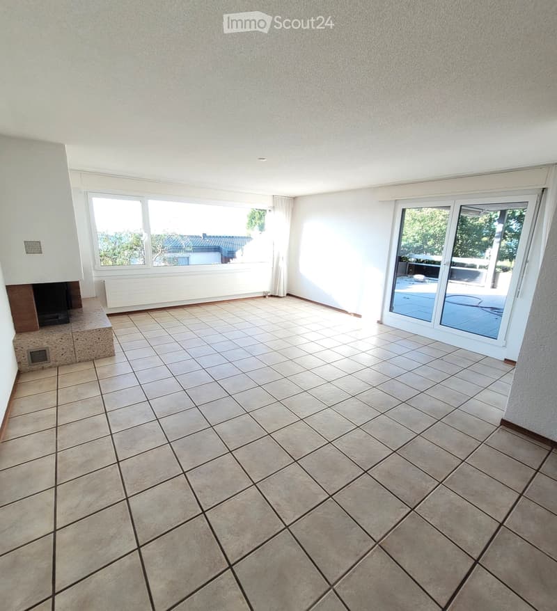 Empty room with tiled floor, fireplace, large windows, and sliding glass door leading to outdoor area.