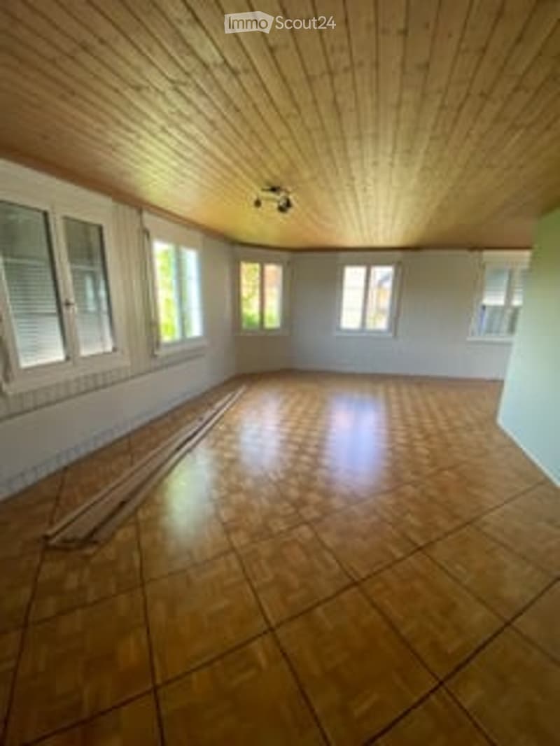 Empty room with wooden floor and ceiling, large windows with white frames, natural lighting.