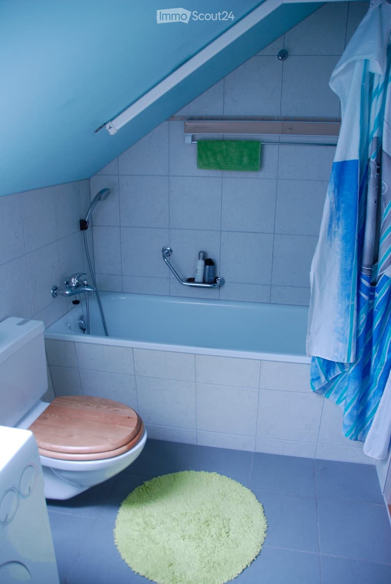 Bathroom with a bathtub, toilet, towel, and a green bathmat on the floor.