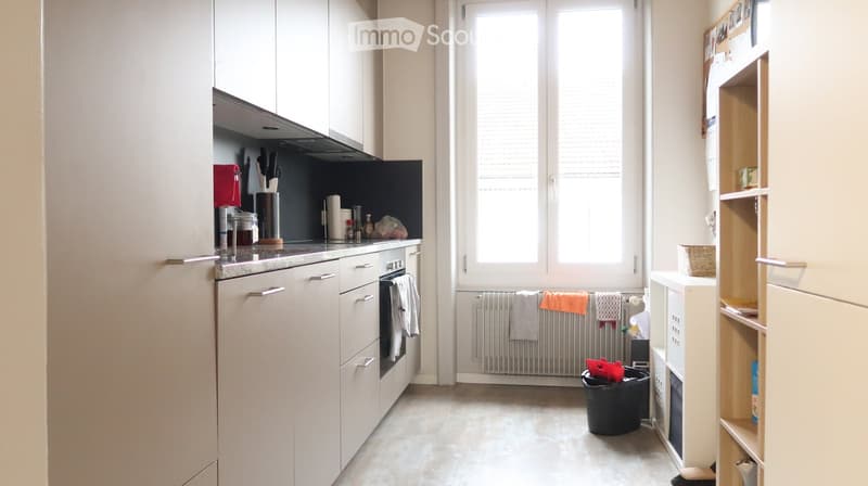 Modern kitchen with white cabinets, stainless steel appliances, and a large window. Includes a coffee maker, knife block, and various kitchen items on the counter.