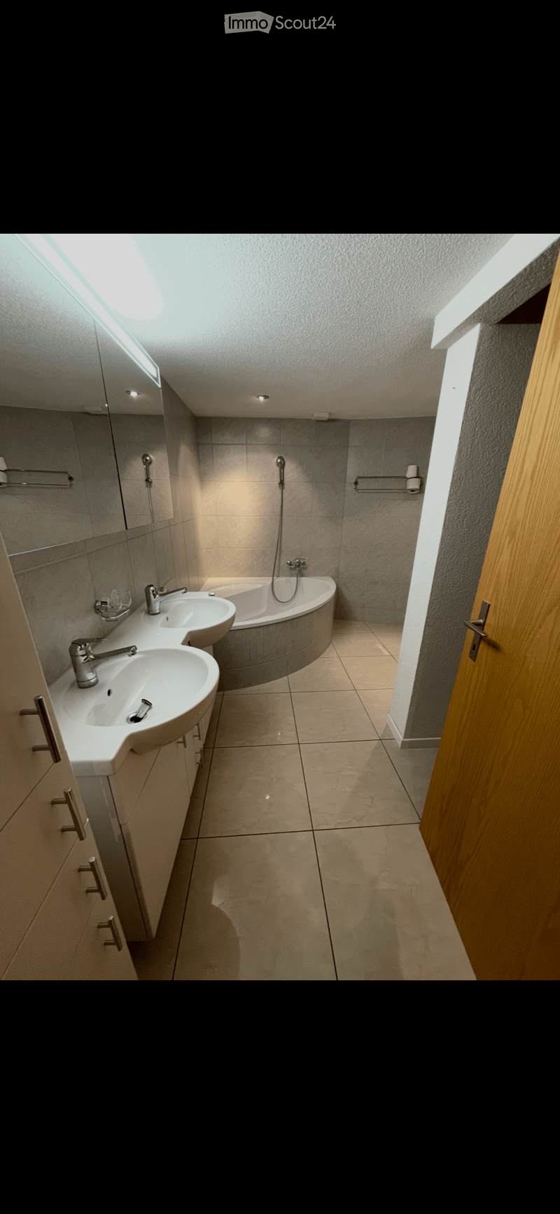 Modern bathroom with two sinks, a bathtub, a mirror, and a towel rack. The space features tiled walls and floor, with sleek, contemporary fixtures.