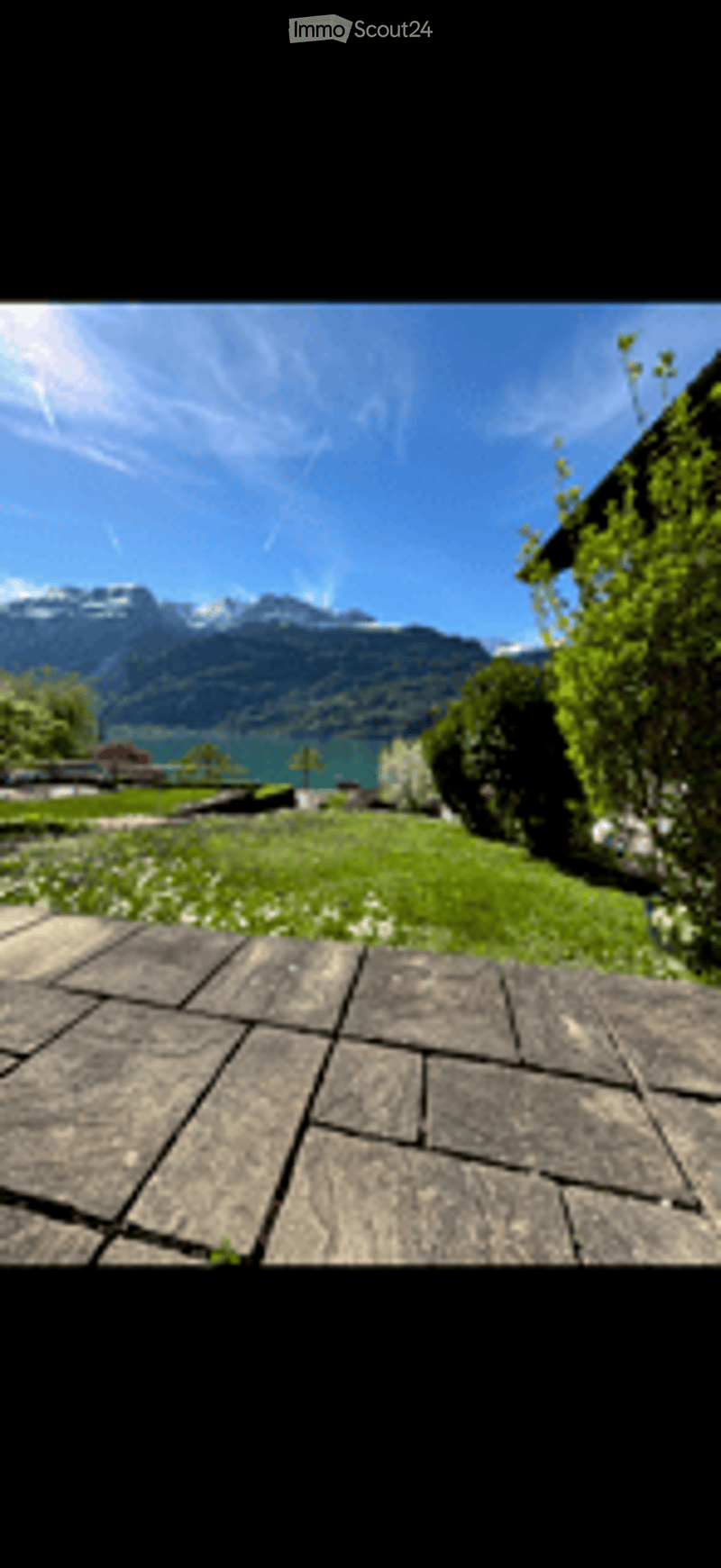 Wooden deck overlooking a green lawn, with a scenic view of mountains and a lake in the background.