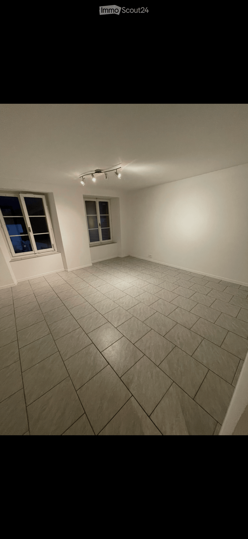 Empty room with light-colored walls, tiled floor, and two windows. No furniture or equipment present.