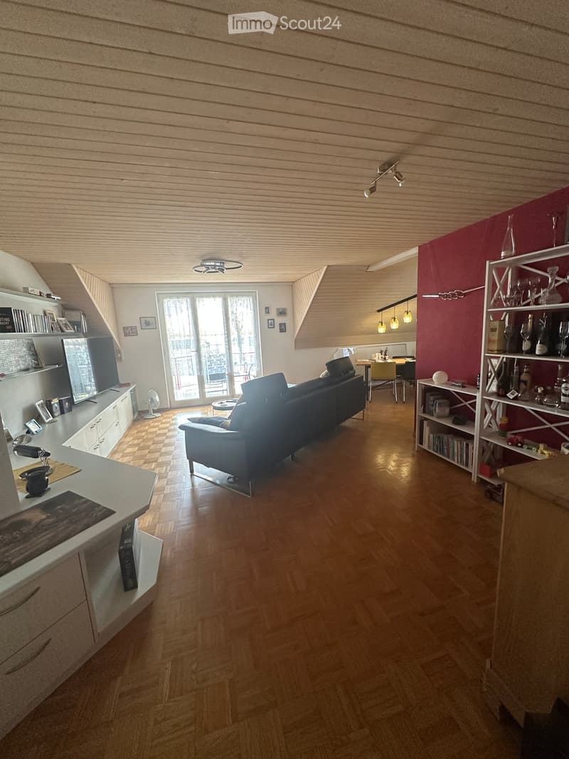 Open-plan living and dining area with wooden flooring, modern furniture, and large windows leading to a balcony.