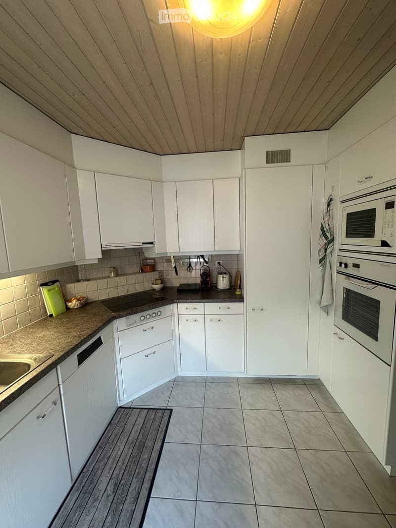 Modern kitchen with white cabinets, stainless steel appliances, and a tiled floor. Features include an oven, microwave, dishwasher, and a countertop with various small appliances and utensils.