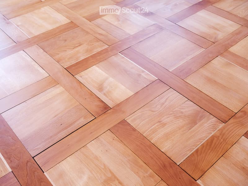 Close-up view of a wooden floor with herringbone pattern in shades of light and dark brown.