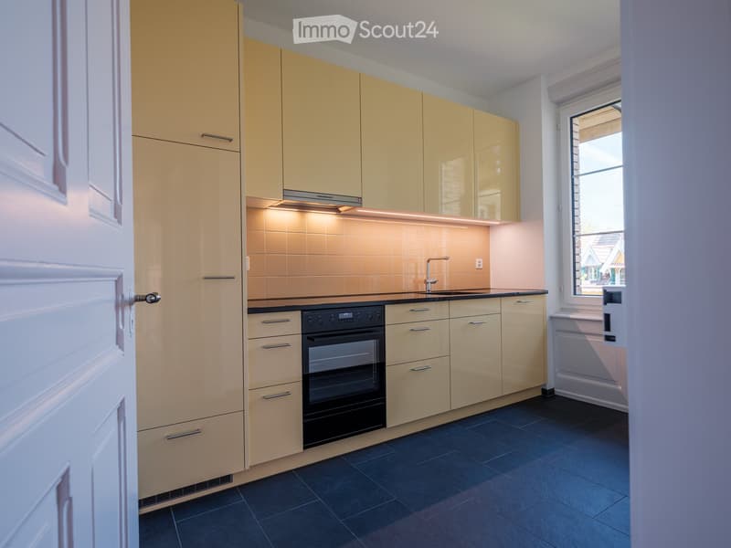 Modern kitchen with light-colored cabinets, a built-in oven, and a sleek faucet, featuring a window with a view of the outside.