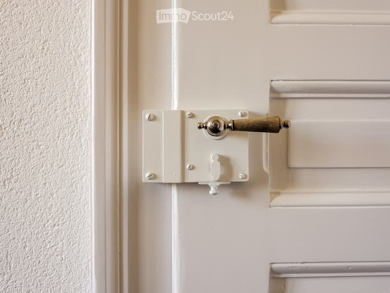 Close-up of a white door handle with a wooden grip attached to a white door frame, set against a textured wall and white louvered paneling.