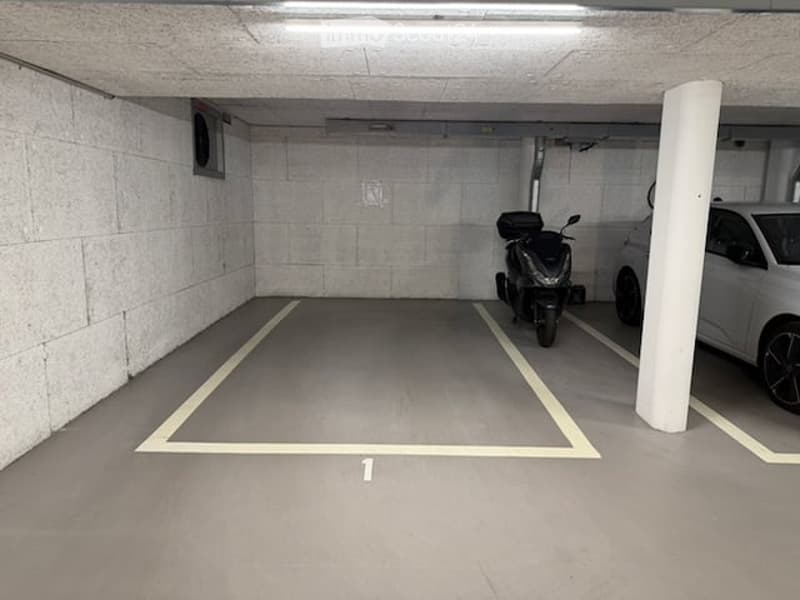 Underground parking space with marked parking spots, a scooter, and a car parked inside.