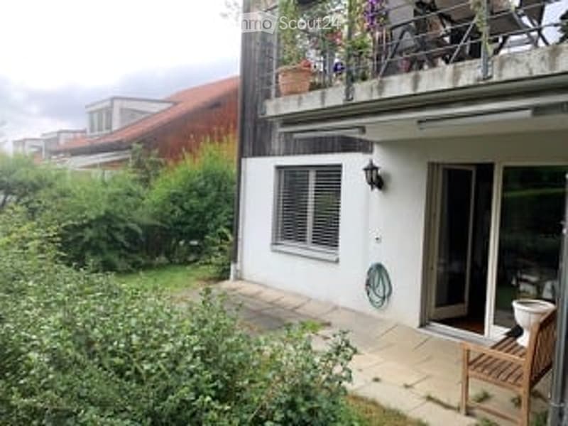 Balcony with outdoor furniture, potted plants, and a view of the garden. The balcony is accessible via a sliding glass door from the interior.