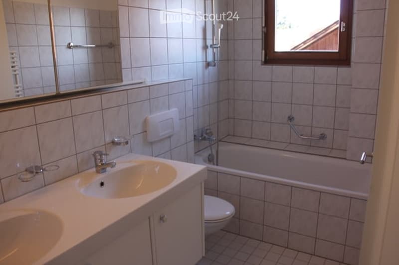 Bathroom with two sinks, a bathtub, and a toilet. The walls are tiled, and there is a large mirror above the sinks.