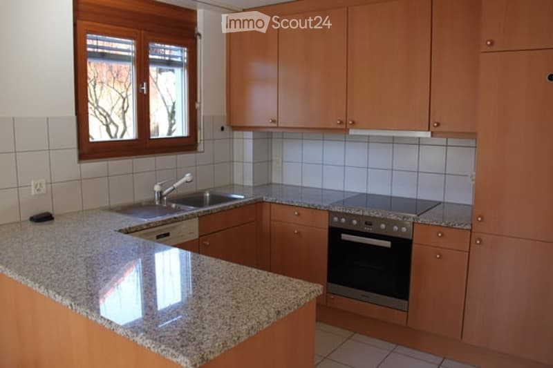 Modern kitchen with light wooden cabinets, granite countertop, stainless steel sink and oven, and a window with wooden frame.