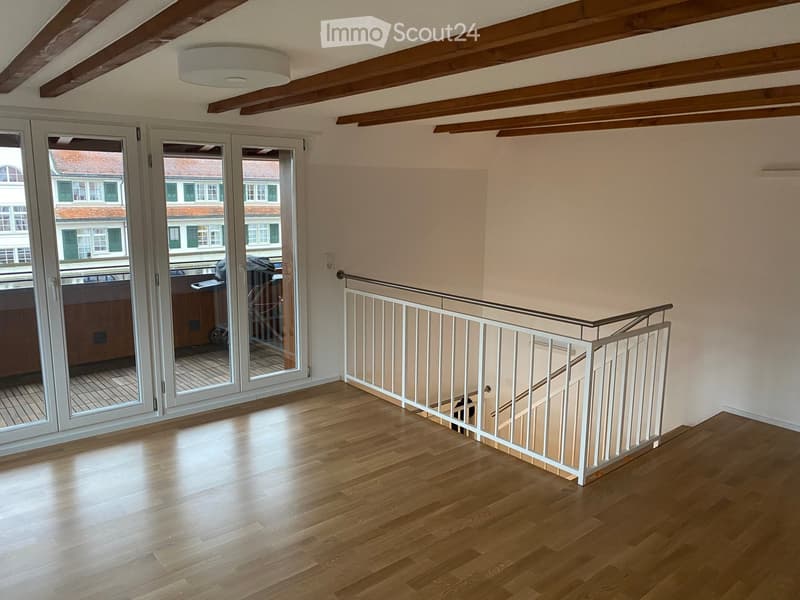 Bright hallway with wooden flooring, white railing, and large glass doors leading to a balcony or outdoor area.